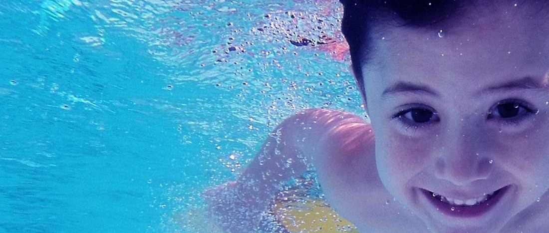 Lachende jongen zwemt onder water in Zwembad Oosterbeek